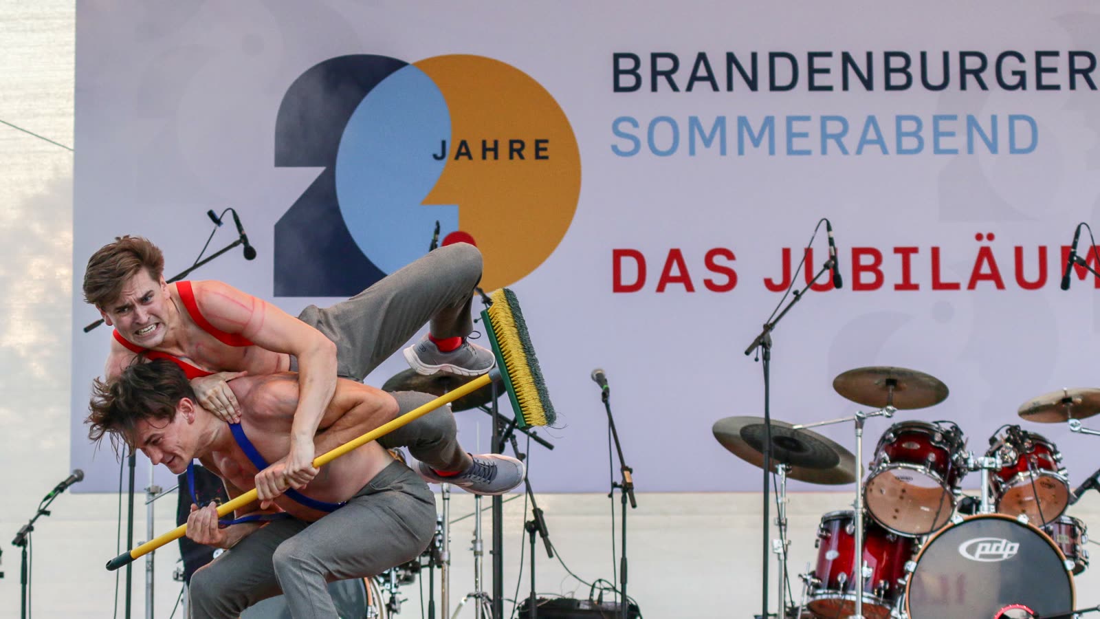 Jim & John beim Bühnenfeger-Act auf der Open-Air-Bühne des Brandenburger Sommerabends zum 20-jährigen Jubiläum, im Hintergrund das Banner der Veranstaltung und ein Schlagzeug